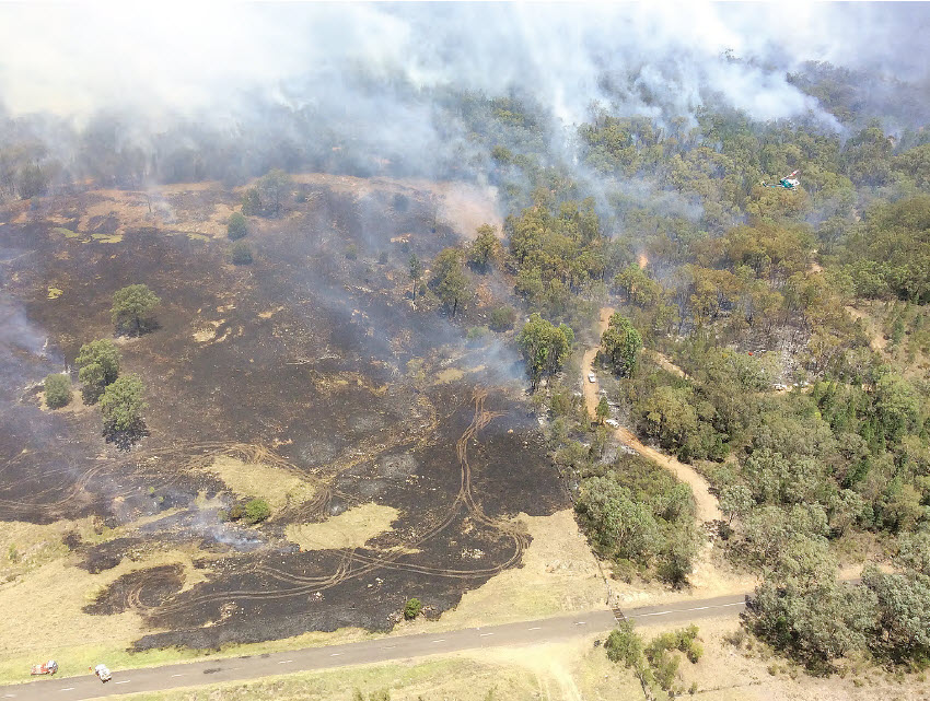 The Bobbiwaa Creek fire, with Killarney Gap road in the foreground. To the right of the picture is a helicopter, dropping water on the fire.
