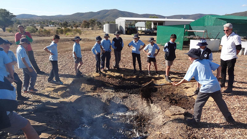 Bingara Central School Stage 3 students take turns to ‘damper down’ the flames in the biochar fire pit under the guidance of Dr Ruy Anaya de la Rosa and Adam Blakester.