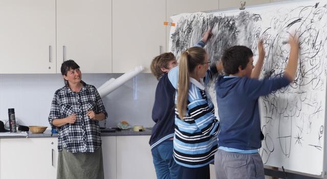 Artist Georgie Pollard watches on while students create a collaborative artwork using charcoal made at TLC.